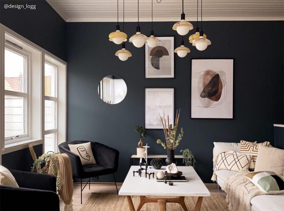 Wohnzimmer mit dunklen Wänden, schwarzen Samtsesseln, rundem Spiegel, grafischen Postern